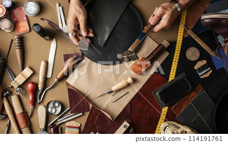 Close up of skinner craftsman working with natural leather using craft tools. Close up of skinner craftsman working with natural leather using craft tools. 114191761
