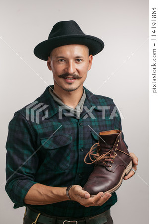 Photo of young cheerful shoemaker holding self made shoe isolated over white. Photo of young cheerful shoemaker holding self made shoe isolated over white. 114191863