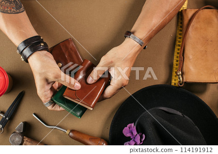 Leather goods master and handmade leather wallets. Workflow in the workshop. 114191912