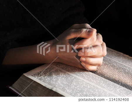 Hands clasped in prayer near an open book Hands clasped in prayer near an open book 114192408