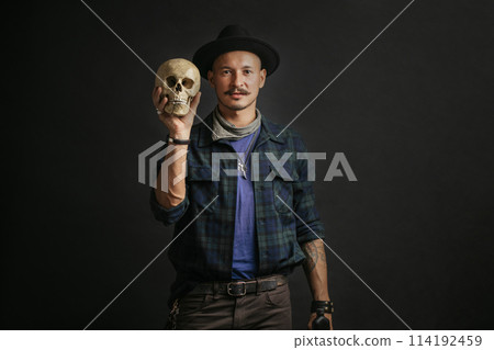 Stylish man with mustache wearing hat and holding scull posing indoors Stylish man with mustache wearing hat and holding scull posing indoors 114192459