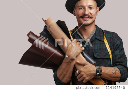 Artisan of leather in creative black hat posing with leather goods in studio. Artisan of leather in creative black hat posing with leather goods in studio. 114192540