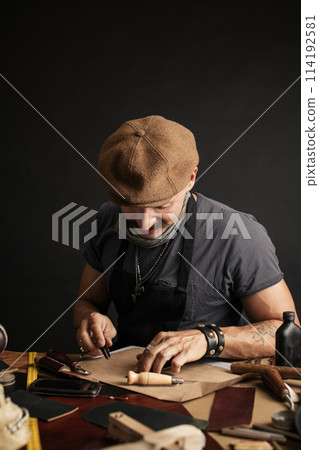Whiskered shoemaker with making measurments in patterns at table in workshop Whiskered shoemaker with making measurments in patterns at table in workshop 114192581