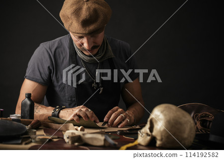 Whiskered shoemaker with making measurments in patterns at table in workshop 114192582