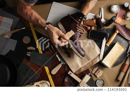 Close up of shoe maker hands producing boots in his leather workshop Close up of shoe maker hands producing boots in his leather workshop 114193091