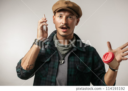 Leather Craftsman using smart phone and holding cup of coffee indoors Leather Craftsman using smart phone and holding cup of coffee indoors 114193192
