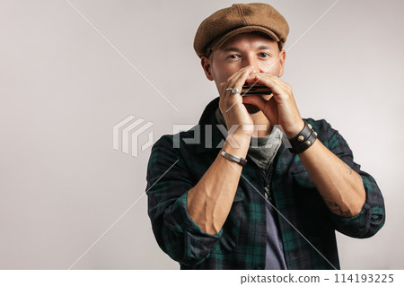 Studio portrait of caucasian moustached man on cap playing harmonica Studio portrait of caucasian moustached man on cap playing harmonica 114193225