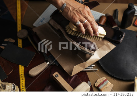 Care for leather shoes, close up of cropped shoemaker hands rubbing up boots 114193232