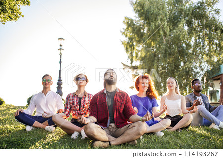 Group of adult mix-race friends meditating while practice yoga outside in park. 114193267
