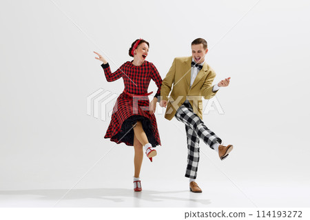 Lovely young couple, man in checkered pants and jacket, woman in red dress energetically dancing isolated over white studio background 114193272
