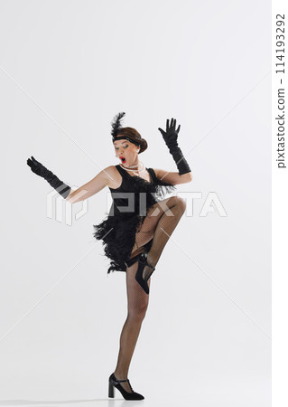 Stylish, young, beautiful woman dressed in 1920s-themed outfit, dancing joyfully isolated over white studio background 114193292