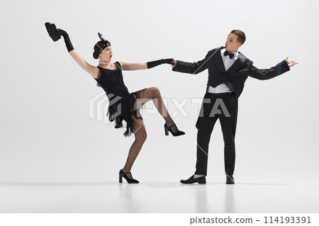 Elegant young couple performing theatrical dance typical of jazz age, demonstrating playful gestures isolated over white studio background 114193391