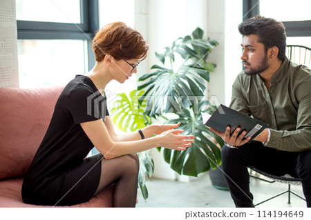 woman is sitting on couch and talking to male indian psychologist while doctor making notes 114194649