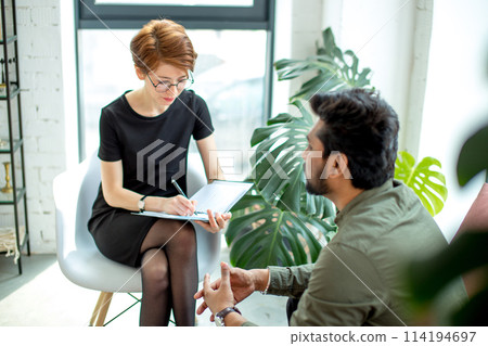 psychologist consulting indian man, writing notes during psychological therapy session 114194697