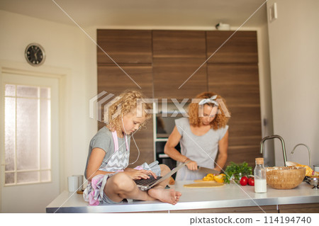 Little girl and her daughter baking cookies at home, reading recipe on laptop. Little girl and her daughter baking cookies at home, reading recipe on laptop. 114194740