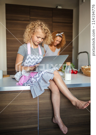 Little girl and her daughter baking cookies at home, reading recipe on laptop. 114194776