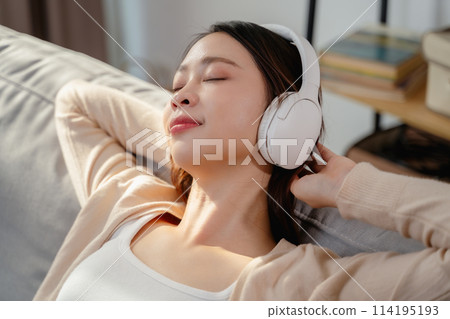 A woman is wearing headphones and laying on a couch 114195193