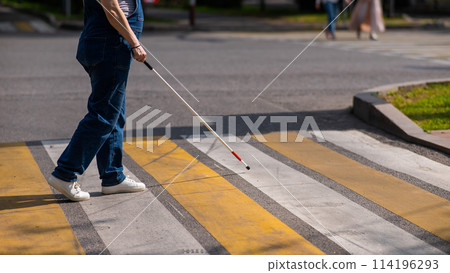 Close-up of the legs of a blind woman crossing the road at a crosswalk with a cane. Close-up of the legs of a blind woman crossing the road at a crosswalk with a cane. 114196293