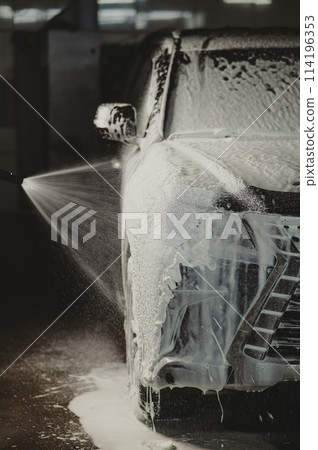 Man applying foam to black car in car wash. Vertical photo.  114196353