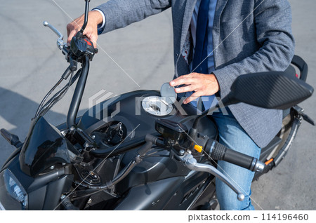 A man opened the charging socket on an electric motorcycle. A man opened the charging socket on an electric motorcycle. 114196460
