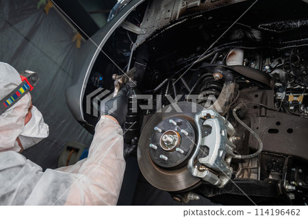 An auto mechanic applies anti-corrosion mastic to the underbody of a car. 114196462