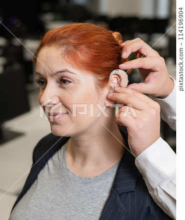 Man putting hearing aid on Caucasian red-haired woman. Man putting hearing aid on Caucasian red-haired woman. 114196904