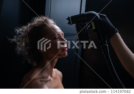 A master applies tinting paint to the face of a Caucasian woman. Instant tanning procedure A master applies tinting paint to the face of a Caucasian woman. Instant tanning procedure 114197082