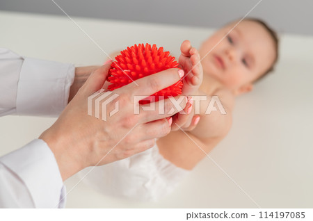 A doctor massages a baby's foot using a spiked ball. A doctor massages a baby's foot using a spiked ball. 114197085