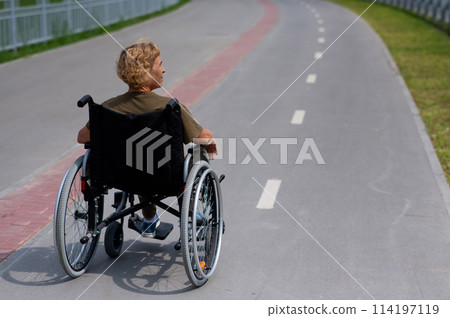 Rear view of an elderly woman in a wheelchair riding on a bike path.  114197119