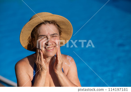 Portrait of an older woman applying sunscreen to her face while on vacation.  114197181