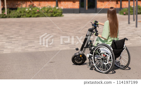 A woman in a wheelchair with an assistive device for manual control. Electric handbike.  114197199