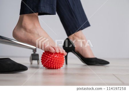 Business woman massages her feet on a massage ball with spikes. 114197258