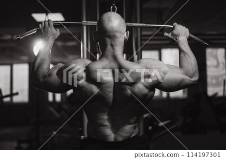 Caucasian man doing lat pull-downs on a machine. Black and white photo.  114197301