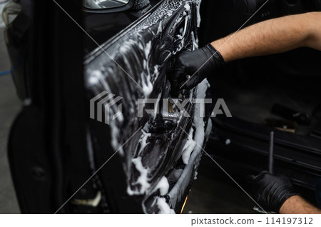 A man cleans the interior of a car with foam and a brush. Clean the door trim. A man cleans the interior of a car with foam and a brush. Clean the door trim. 114197312