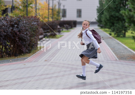 Happy caucasian girl in uniform and with a backpack jumping outdoors after school. Happy caucasian girl in uniform and with a backpack jumping outdoors after school. 114197358