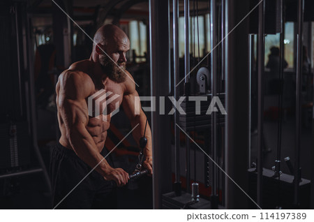 Bald Caucasian Bodybuilder doing heavy triceps exercises with cable.  114197389