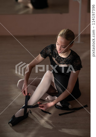 Woman sitting on the floor and tying ribbons on her pointe shoes. Vertical photo.  114197396