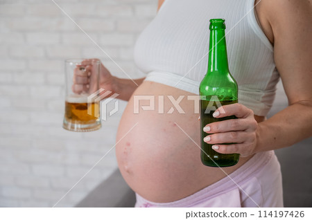 Pregnant woman holding glass and bottle of beer.  114197426