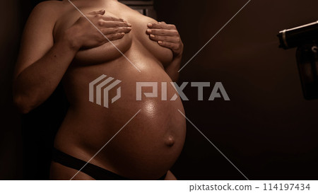 Faceless pregnant woman getting an instant tan. The master applies bronzer with a spray. 114197434