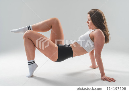 Athletic Caucasian woman in shorts and crop top posing on white background.  114197506