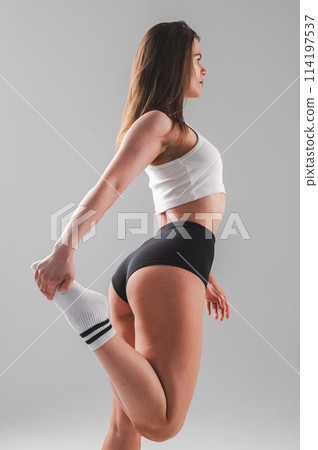 Athletic Caucasian woman stretching her quadriceps on a white background. Vertical photo. 114197537