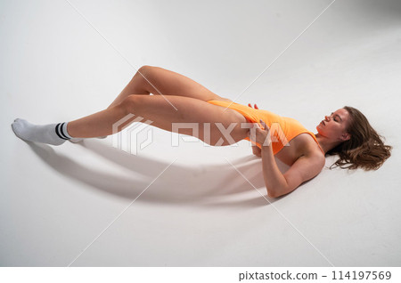 Beautiful athletic woman posing while lying on a cyclorama in an orange bodysuit.  114197569