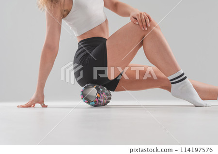 Faceless woman doing roller exercise for myofascial release on white background. Self-massage of thighs.  114197576