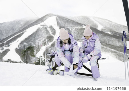 A mother helps her daughter put on ski boots at a ski resort 114197666