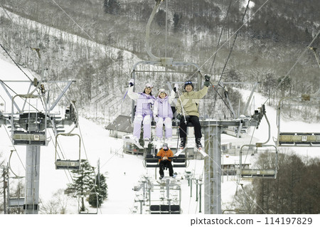 Family, parents and daughter riding a chairlift on a snowy mountain 114197829