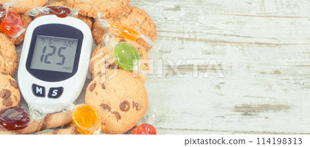 Glucose meter with high sugar level, candies and cookies Glucose meter with high sugar level, candies and cookies 114198313