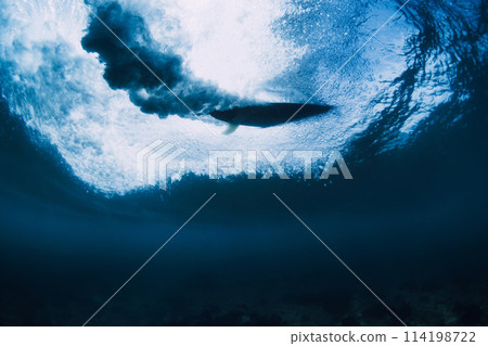 Surfer on surfboard in ocean underwater. Crashing wave and surfboard in transparent water Surfer on surfboard in ocean underwater. Crashing wave and surfboard in transparent water 114198722