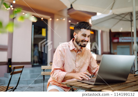 Smiling young man working in cafe on street with laptop and phone. Freelance business concept. 114199132