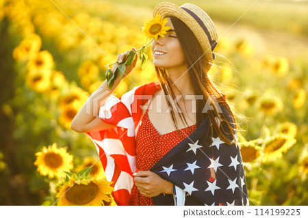 Beautiful girl in hat with the American flag in a sunflower field. 4th of July. Fourth of July. Freedom 114199225