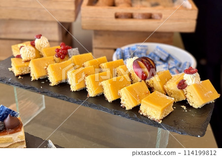 The portions of yellow layered cream cake with red currant on a black stands on the counter of the restaurant. Close-up The portions of yellow layered cream cake with red currant on a black stands on the counter of the restaurant. Close-up 114199812